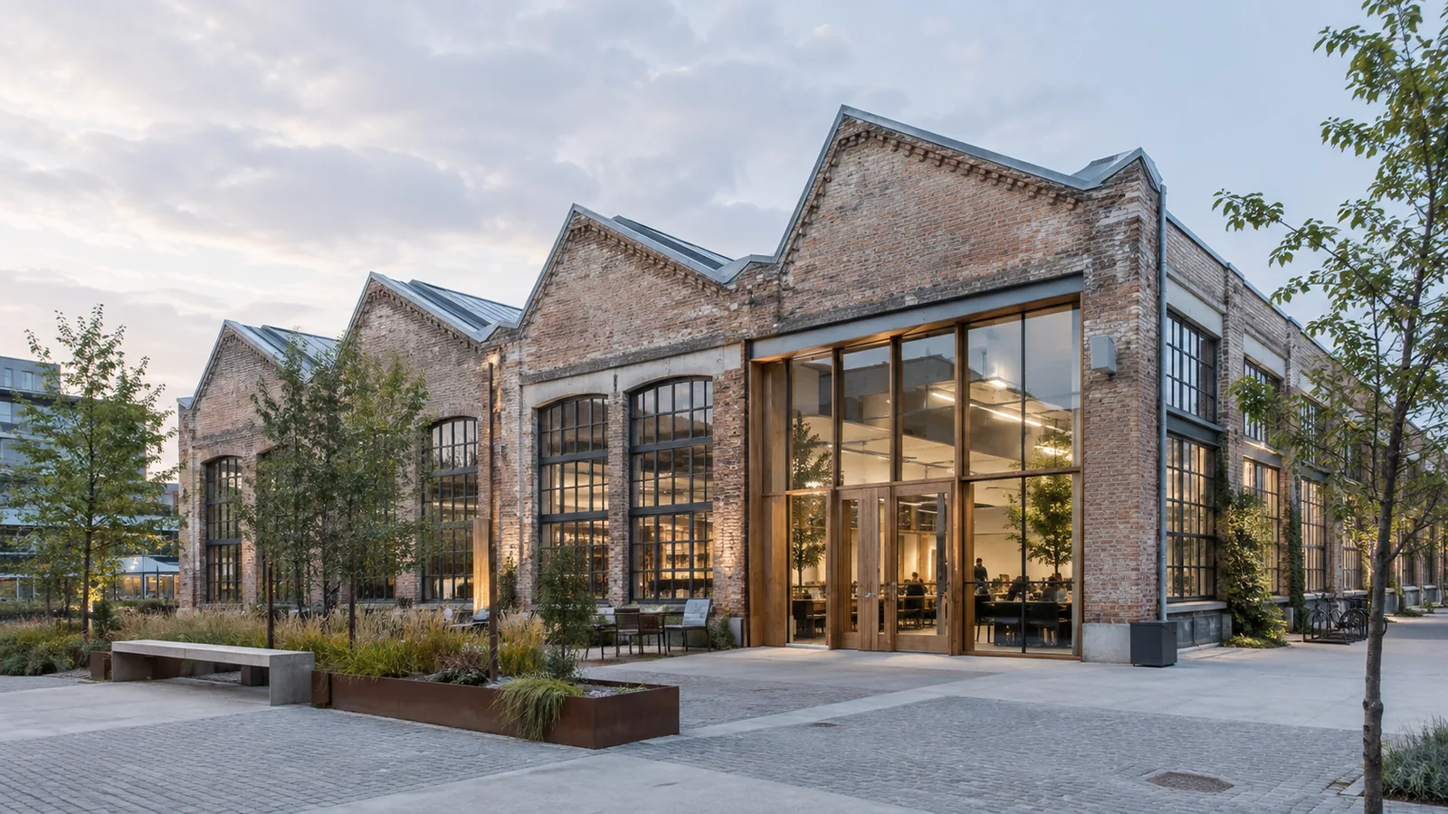 Illustration d’une ancienne halle industrielle en brique reconvertie, avec toiture en sheds et nouveaux espaces vitrés.